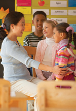 Female teacher supportively holds arms of young girl as a boy and girl look on.